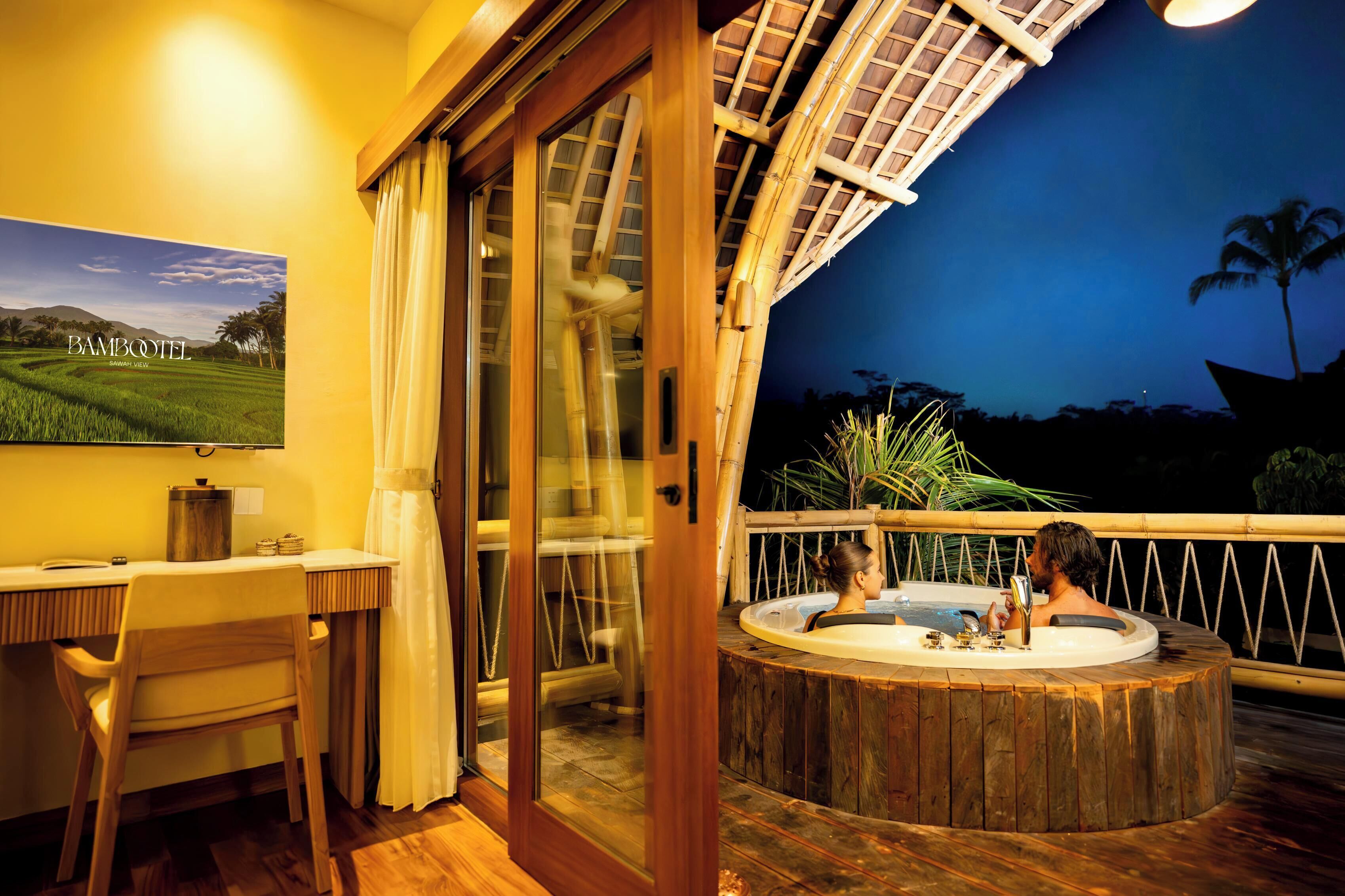 A room with a large window, a desk, a chair, and a hot tub.
