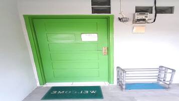 Una porta verde con un tappetino d'ingresso, una piccola finestra e una presa elettrica sulla parete.