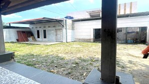 Un cortile con un'area salotto coperta, un edificio con tetto in metallo e una recinzione con materiali da costruzione.