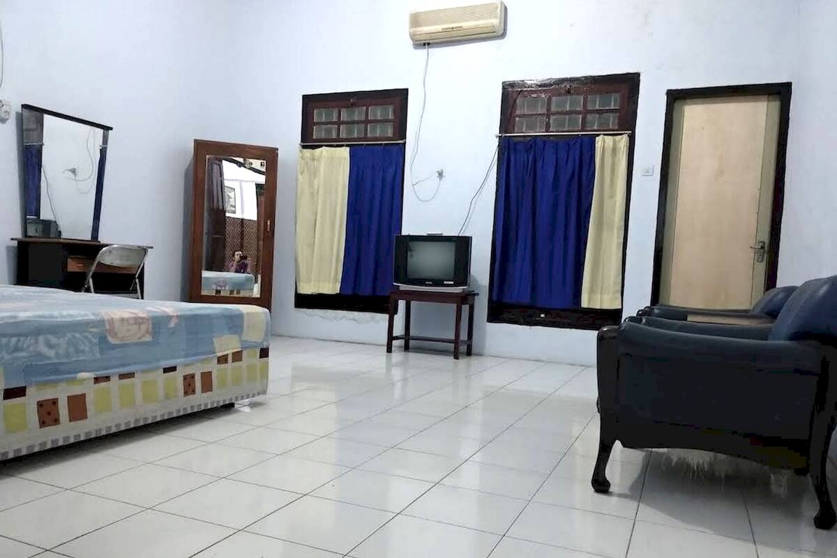 A room with a bed, a chair, a television, and two windows with curtains.