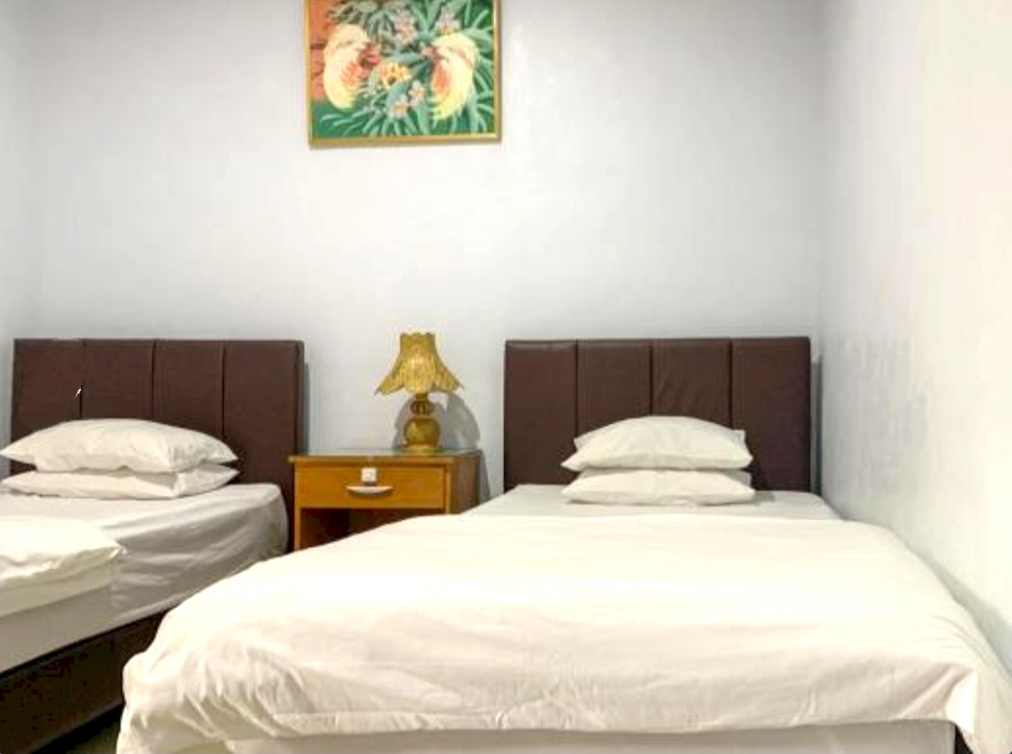 Camera d'albergo con due letti, un comodino con una lampada e un quadro appeso al muro.