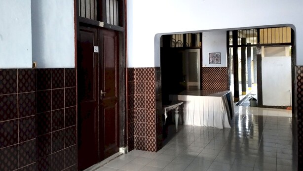 A hallway with a door, patterned tiles, a table with a white tablecloth, and a staircase leading to another room. - Hotel O Mareje Sariguna (Mataram)