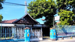 A gated entrance with a metal fence and blue pillars, leading to a building with a red roof. - Hotel O Mareje Sariguna (Mataram)
