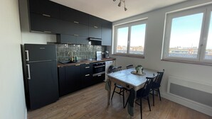 A modern kitchen with dark cabinetry, a wooden dining table, and a view through large windows. - The Lighthouse (Calais)