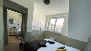 A bedroom with a bed, a window, a coat rack, and a view of the city. - The Lighthouse (Calais)
