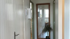 A hallway with a white door, a telephone, a mirror, and a potted plant. - The Lighthouse (Calais)