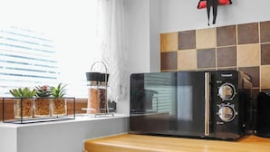 A kitchen with a black microwave, a wooden countertop, and a window with plants.