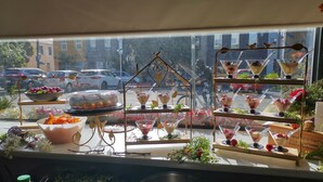 Un étal de nourriture où sont présentés divers desserts dans des récipients en verre transparent, un saladier rempli de fruits et un oiseau décoratif posé sur un présentoir.
