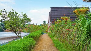 A pathway flanked by lush greenery and flowering plants, leading to a building with a dark roof. - Collection O 92634 Villa Ds (Rancakalong)