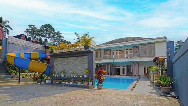 A pool area with a water slide, potted plants, and a two-story building with balconies. - Collection O 92634 Villa Ds (Rancakalong)