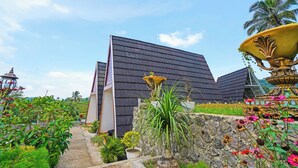 A modern building with a sloped roof, surrounded by a garden with various plants and a large decorative urn. - Collection O 92634 Villa Ds (Rancakalong)