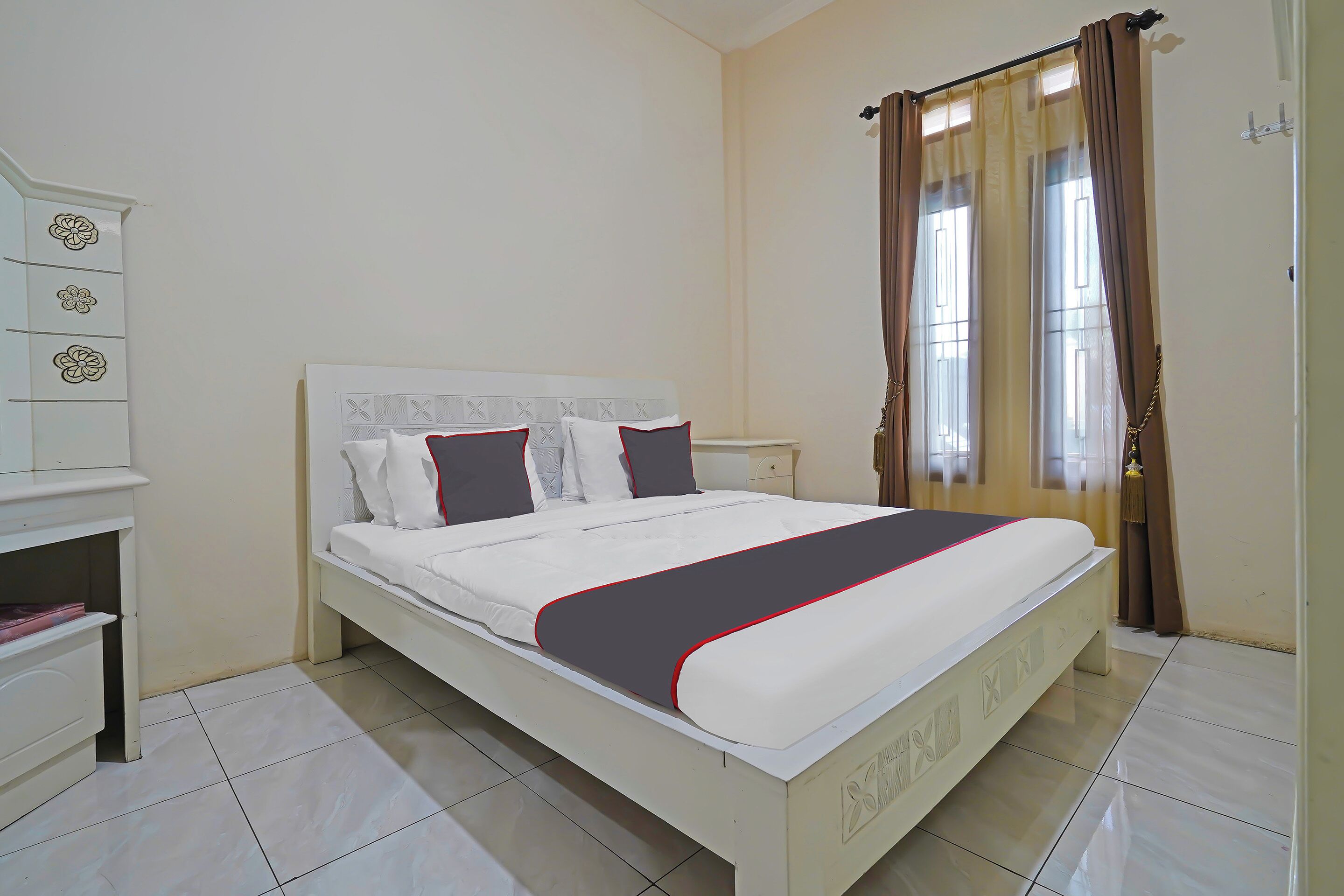 A neatly made bed with a white headboard, a bedside table, and a wardrobe with floral designs.