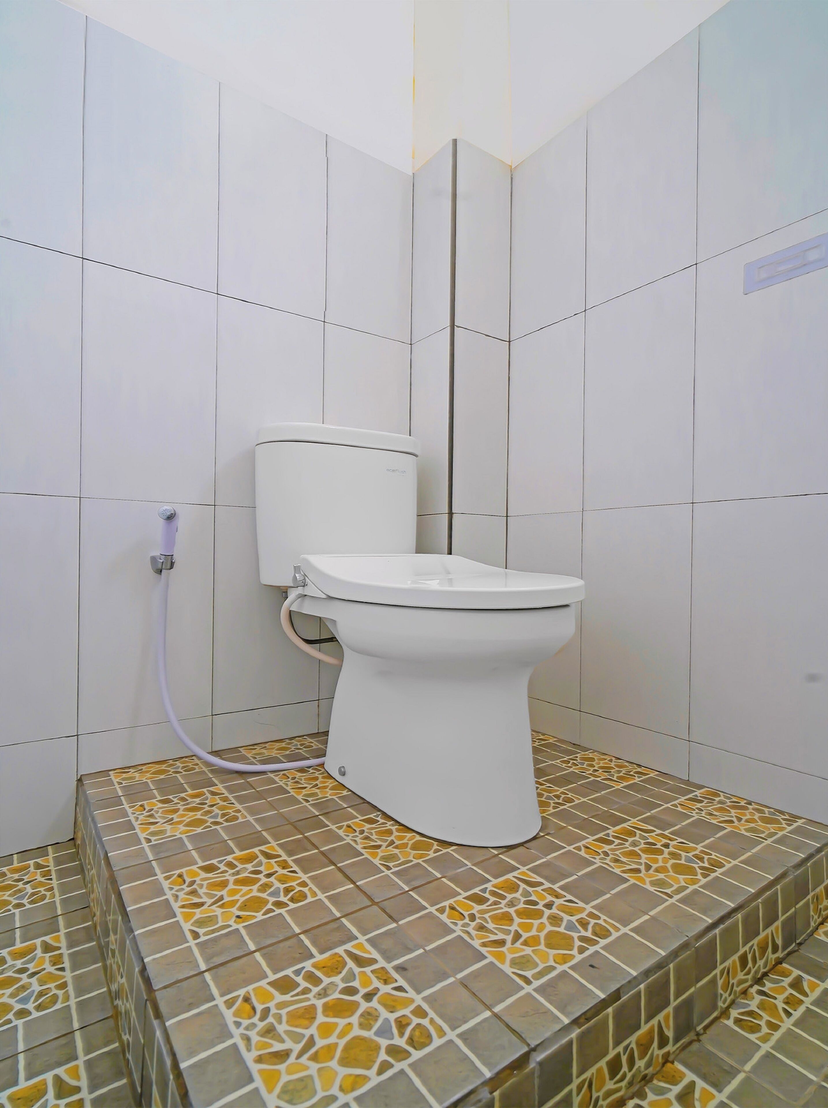 Des toilettes dans une salle de bain aux murs recouverts de carreaux blancs et au sol orné de mosaïques.