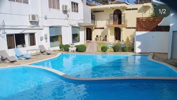 Una piscina con sillones de descanso y un edificio al fondo.