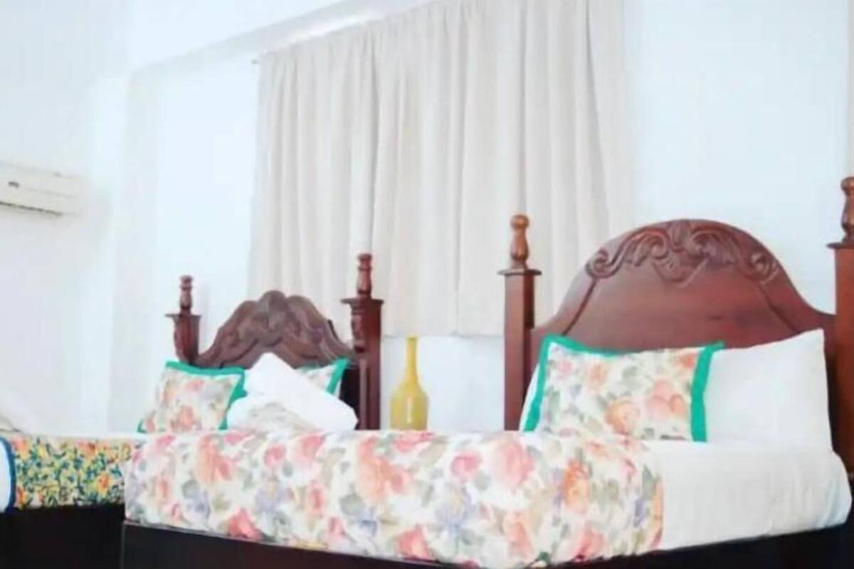 A bedroom with a wooden bed, floral bedding, and a window with curtains.
