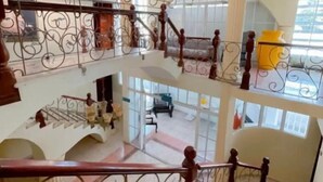 Un interior de varios niveles con barandillas decorativas, ventanas amplias y una imponente escalera.