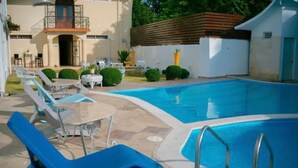 Una piscina con sillas de descanso y una mesa, rodeada por un edificio blanco con un balcón.