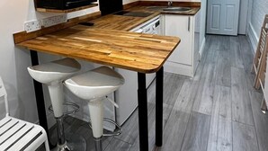A modern kitchen with a wooden island, two bar stools, a microwave, and a sink. - Spacious 3 Bed Flat in Greenwich for 6 (London)
