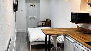 A compact kitchen with a wooden countertop, a microwave, and a sink. There is a small dining area with a table and chairs. - Spacious 3 Bed Flat in Greenwich for 6 (London)