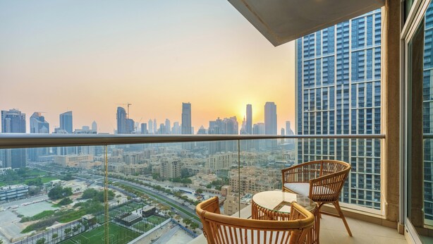 Een balkon met rieten stoelen en een tafel, met uitzicht op een stadsbeeld met gebouwen en een sportveld.