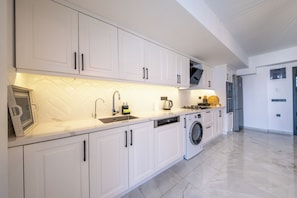 A modern kitchen with white cabinetry, a built-in dishwasher, a washing machine, and a stainless steel refrigerator.