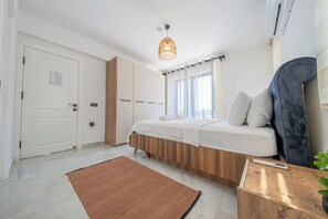 Un dormitorio moderno con una cama, una mesita de noche de madera, un aire acondicionado de pared y una lámpara del techo.
