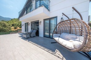 Een modern gebouw met een balkon, een hangstoel en een tafel met stoelen.