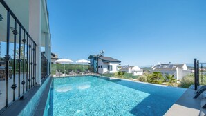 Una piscina azul cristalina con vistas a casas y montañas al fondo.