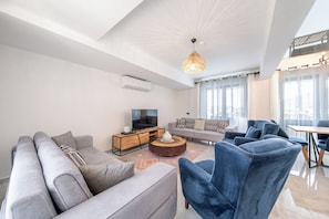 A modern living room with a sofa, armchairs, a coffee table, and a television.