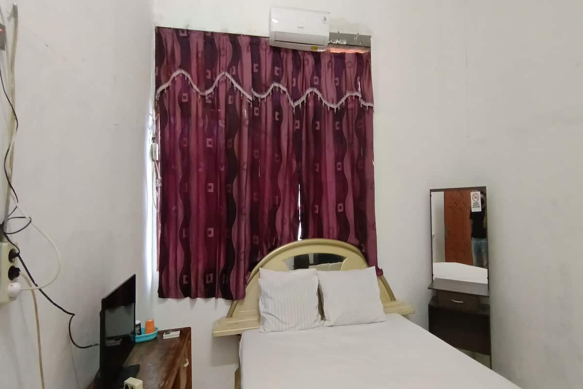 A bedroom with a bed, a bedside table, a mirror, and a window with curtains.