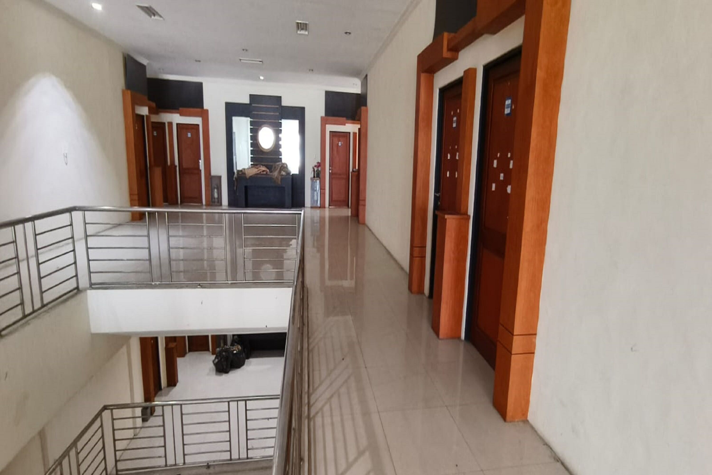 Pasillo de hotel con balcón en el segundo piso, puertas de madera y un ventanal circular central.