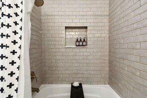 Ein Badezimmer mit einer weißen Badewanne, einem schwarzen Duschvorhang mit Kreuzmuster und einem Regal mit drei Flaschen.