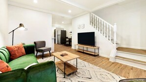 A modern living room with a green sofa, a coffee table, a TV on a stand, and a staircase.