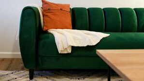 A green sofa with a white throw blanket and an orange pillow.