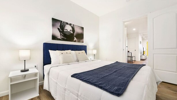A modern bedroom with a large bed, white bedding, a blue headboard, and a framed picture on the wall.