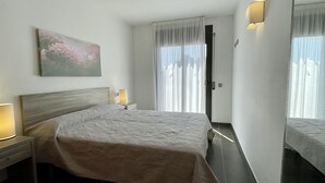 Quarto de hotel com cama, luminárias de cabeceira, um quadro, uma porta e uma janela com cortinas.