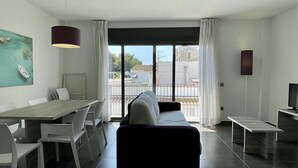 Uma sala de estar moderna com sofá, mesa de jantar com cadeiras, televisão e varanda com vista para prédios.