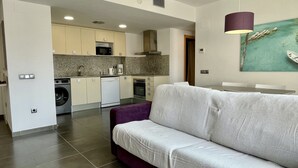Uma cozinha moderna com eletrodomésticos embutidos, um espaço de refeições com uma mesa e uma sala de estar com um sofá.