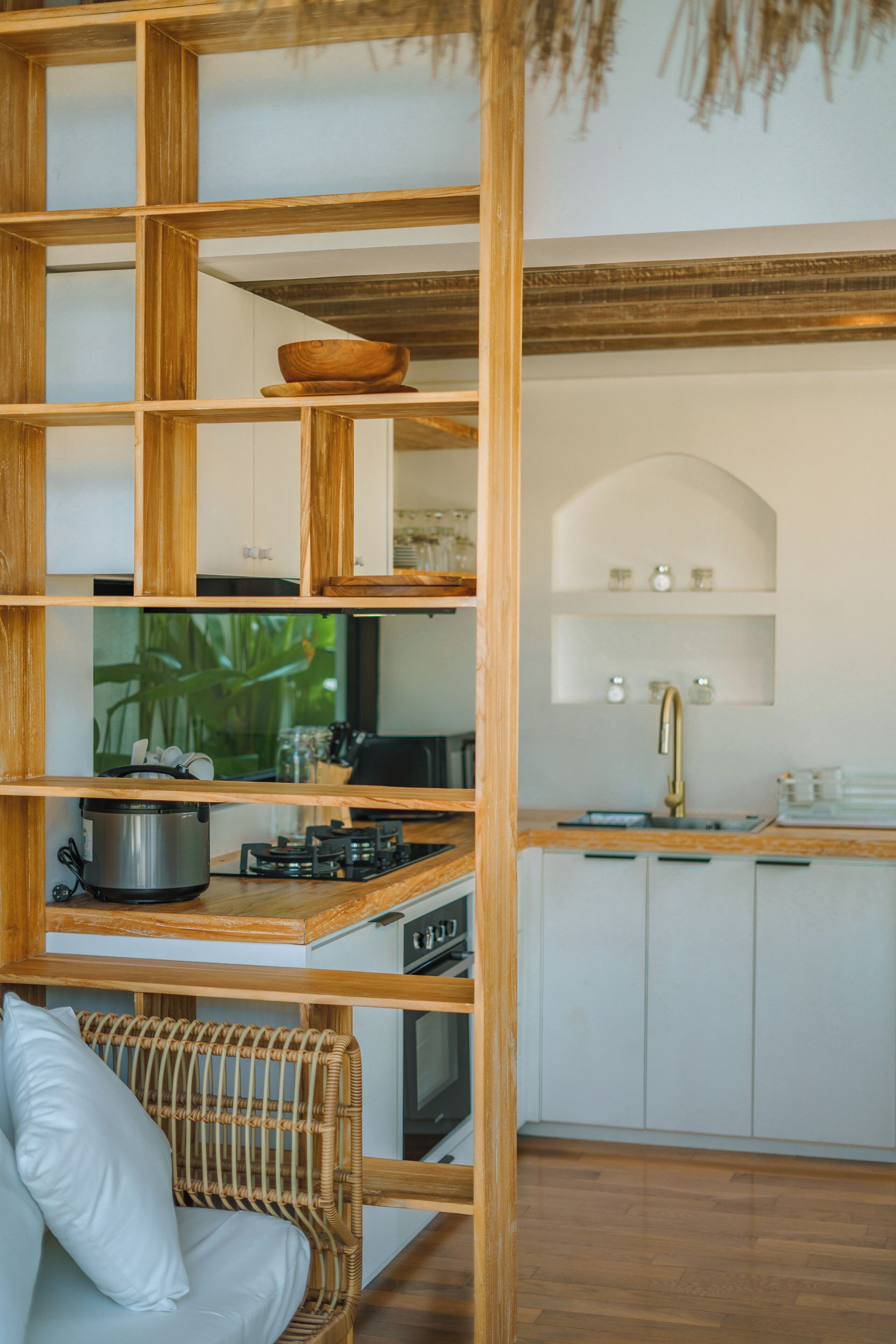 Una cocina con estantes de madera, una silla de mimbre y un armario blanco.