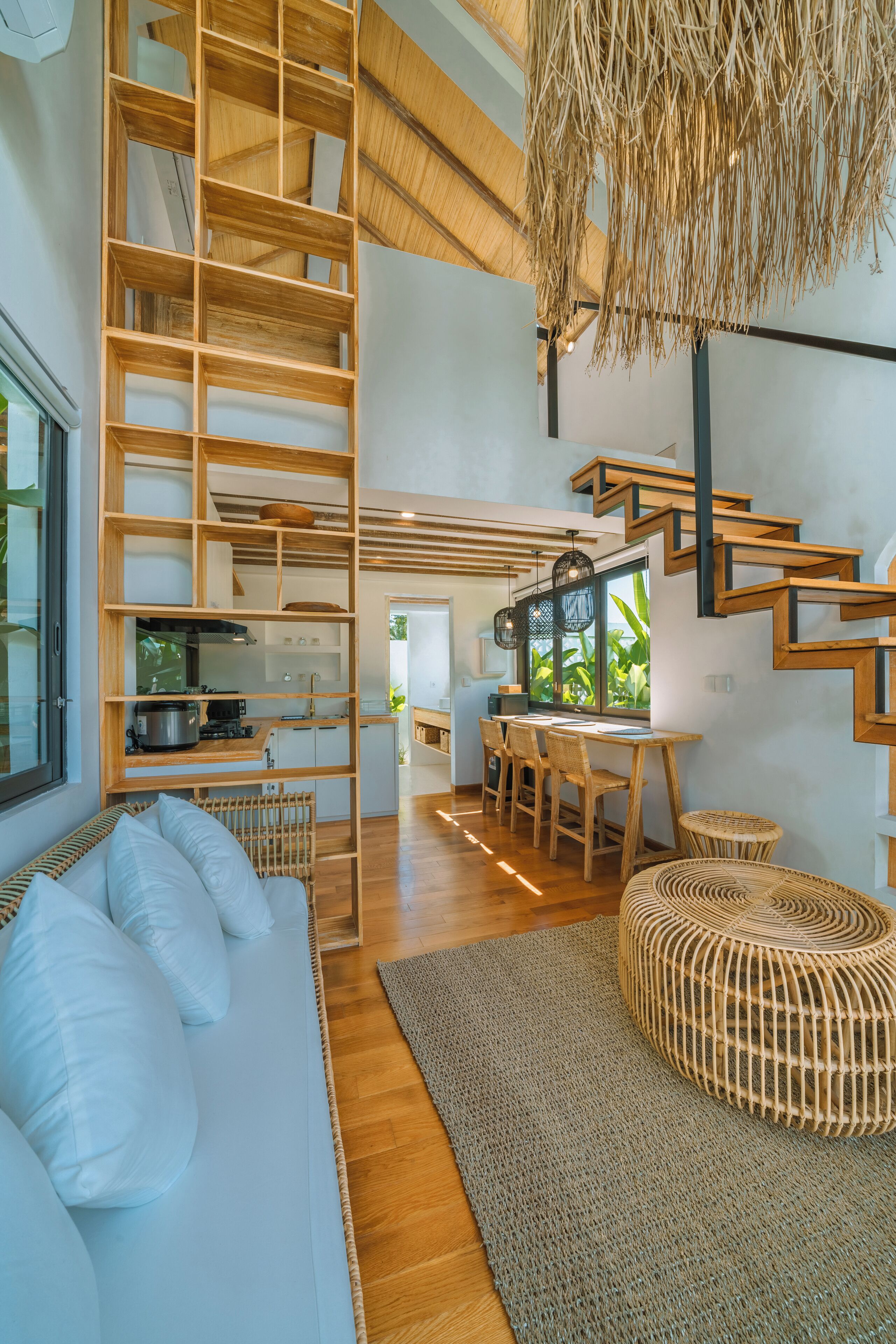 Ein modernes Interieur mit einer Holztreppe, einer Küchenzeile, einem Esstisch mit Stühlen und einer Sitzecke inklusive Sofa und Hocker.