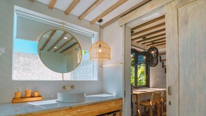 Un baño con techo de madera, un espejo grande, un lavamanos blanco y cestas de mimbre.