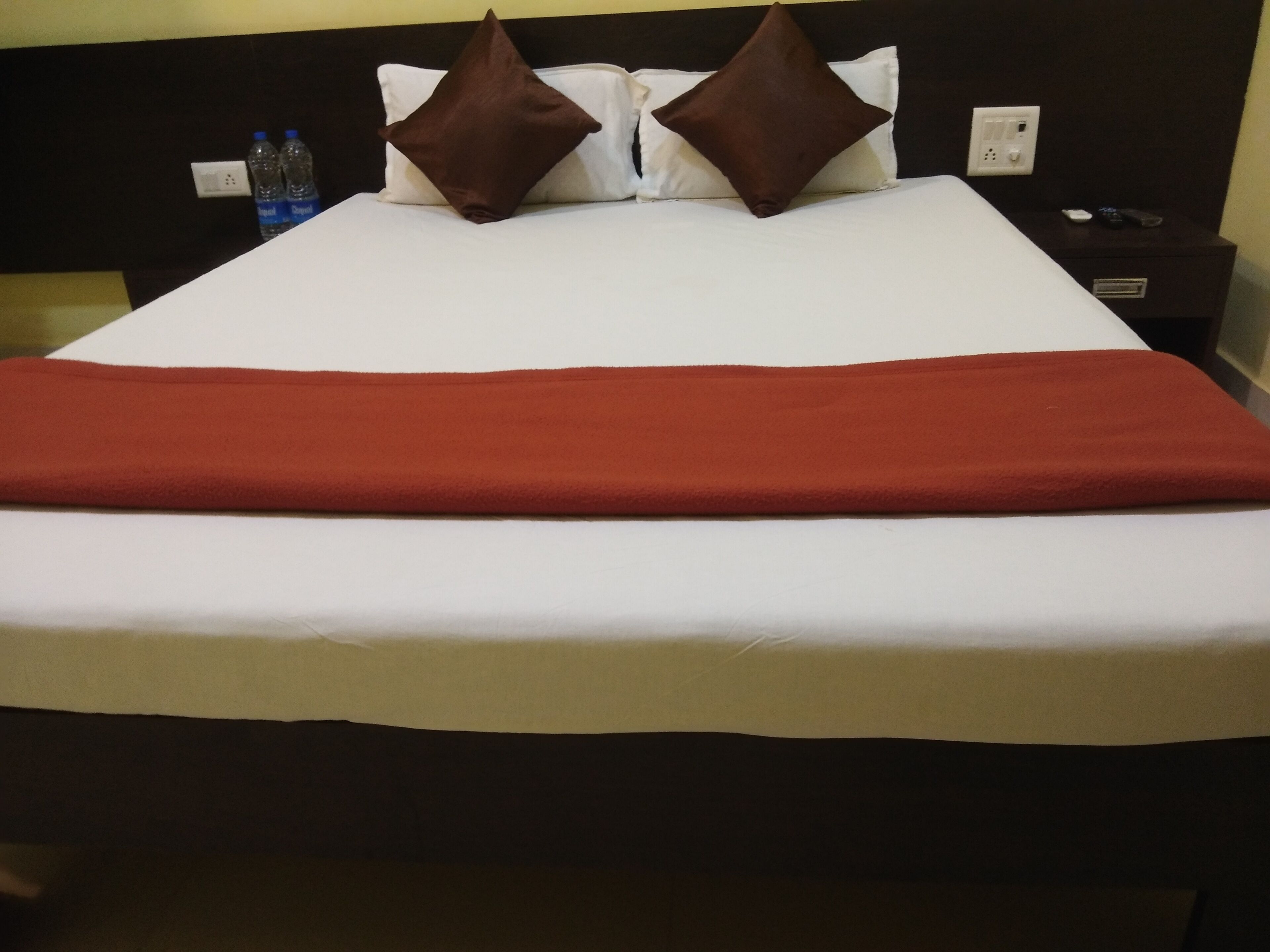Un letto rifatto con una coperta rossa, due cuscini marroni e un piumone bianco.