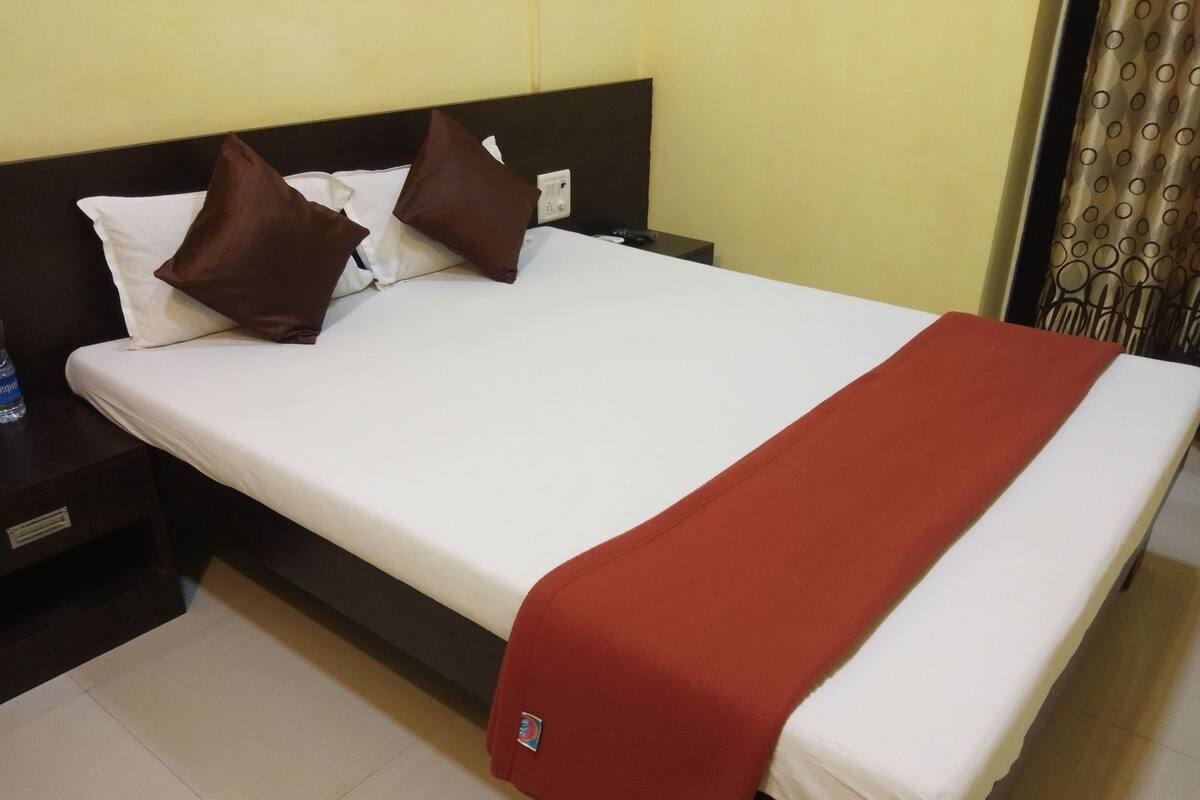 Una habitación de hotel con una cama, una mesita de noche, una botella de agua y una manta roja.