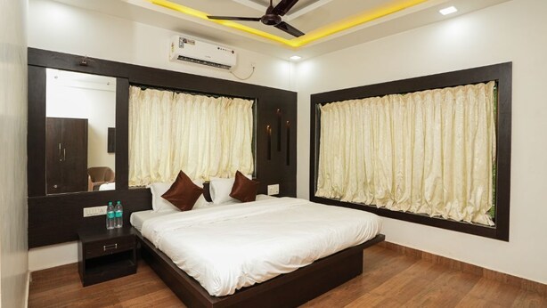 A modern bedroom with a large bed, dark wooden headboard, a ceiling fan, and a large window with curtains.