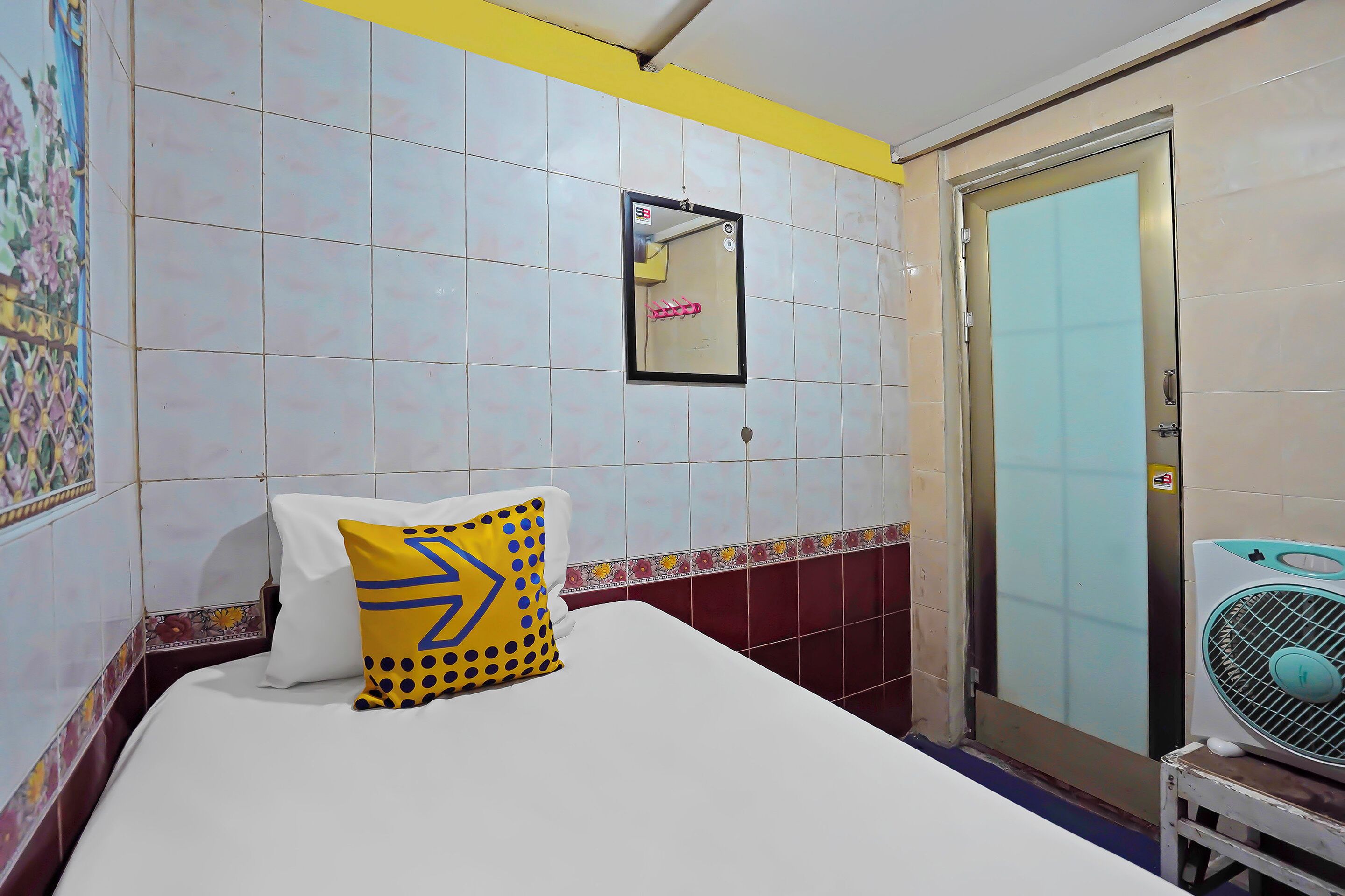 A hotel room with a bed, a mirror, a door, and a fan.