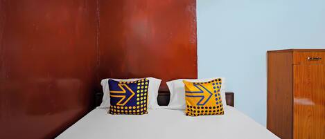 A hotel room with a bed, two pillows with arrow patterns, a wooden wardrobe, and an air conditioning unit.