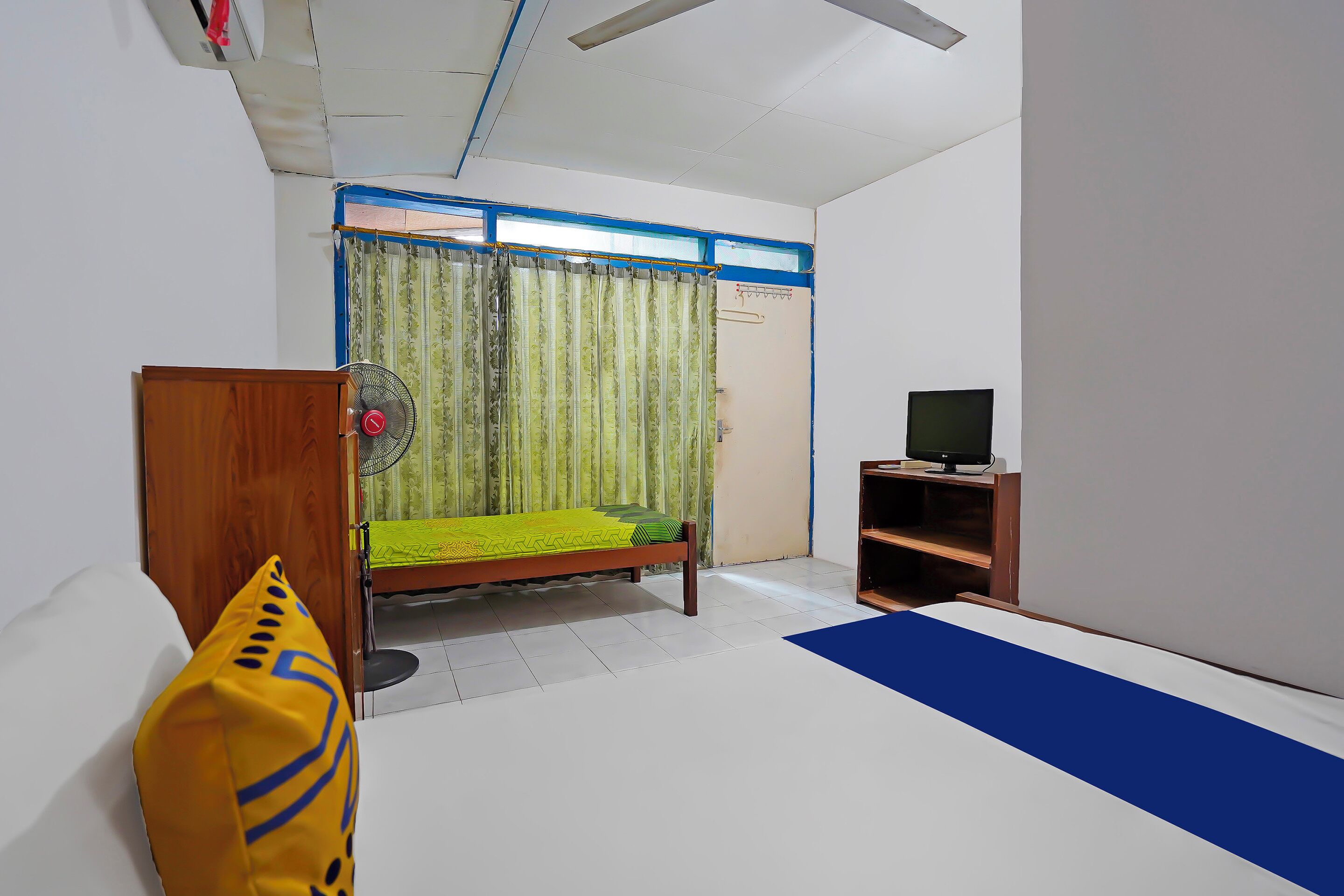 A bedroom with a bed, a TV, a fan, and a wooden wardrobe.
