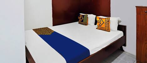 Una cama con colcha azul y blanca, dos almohadas con diseños geométricos y un cabecero de madera.
