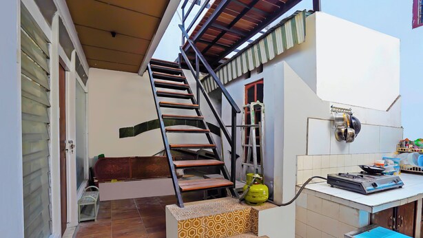 A staircase leading to a second floor, a small table with a gas cylinder, and a window with blinds. - OYO Life 92651 Meir E-homestay Syariah (Surabaya)