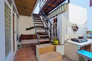 A staircase leading to a second floor, a small table with a gas cylinder, and a window with blinds. - OYO Life 92651 Meir E-homestay Syariah (Surabaya)